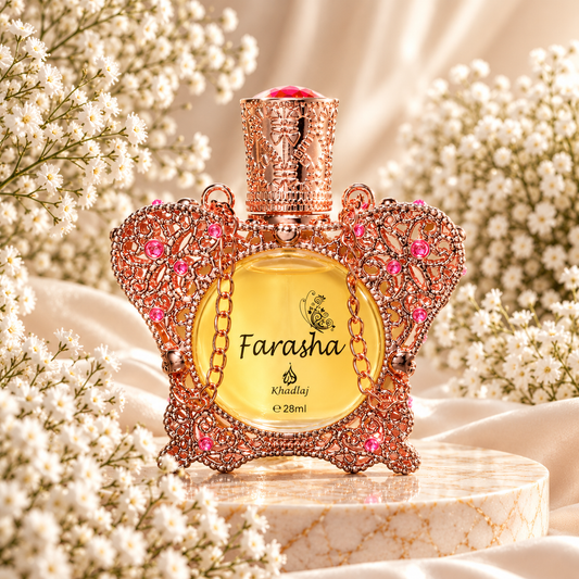 Frasco de óleo perfumado Farasha Khadlaj 28 mL, com estrutura trabalhada em forma de borboleta, acabamento dourado rosado e pedras cor-de-rosa, sobre mármore e rodeado de pequenas flores brancas.